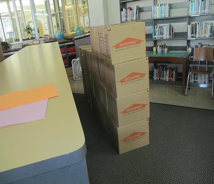 Cardboard boxes with the SERVPRO logo in the center of the room are stacked in 4 rows in a library. 