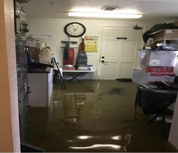 A storage room with vacuums and a huge clock in the back has been flooded with grey water. 
